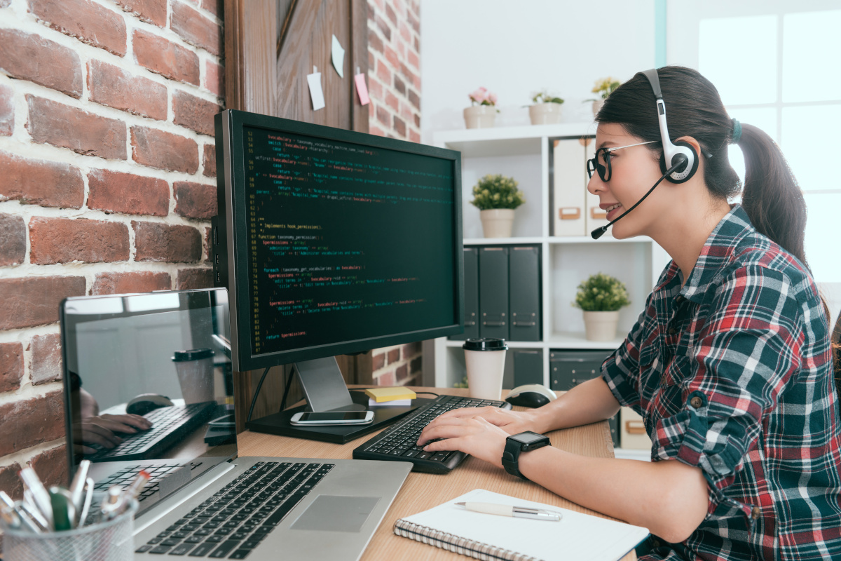 A man woman wearing a headset while working on code in her home office 