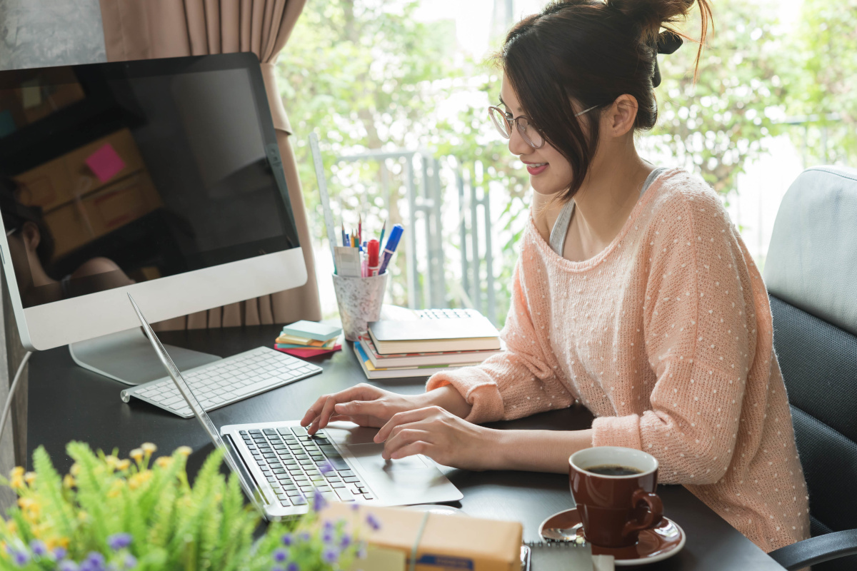 A woman in a sweeter working at on her laptop at her office desk at home