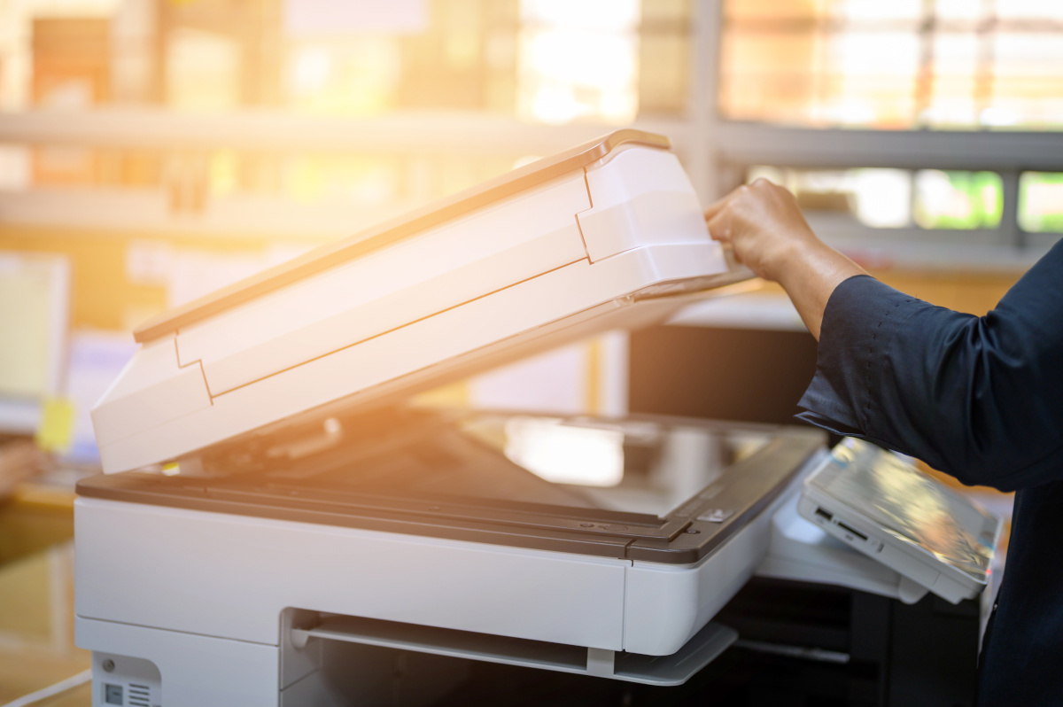 A close up of a copier being opened as light from a sunset comes in through the window behind it